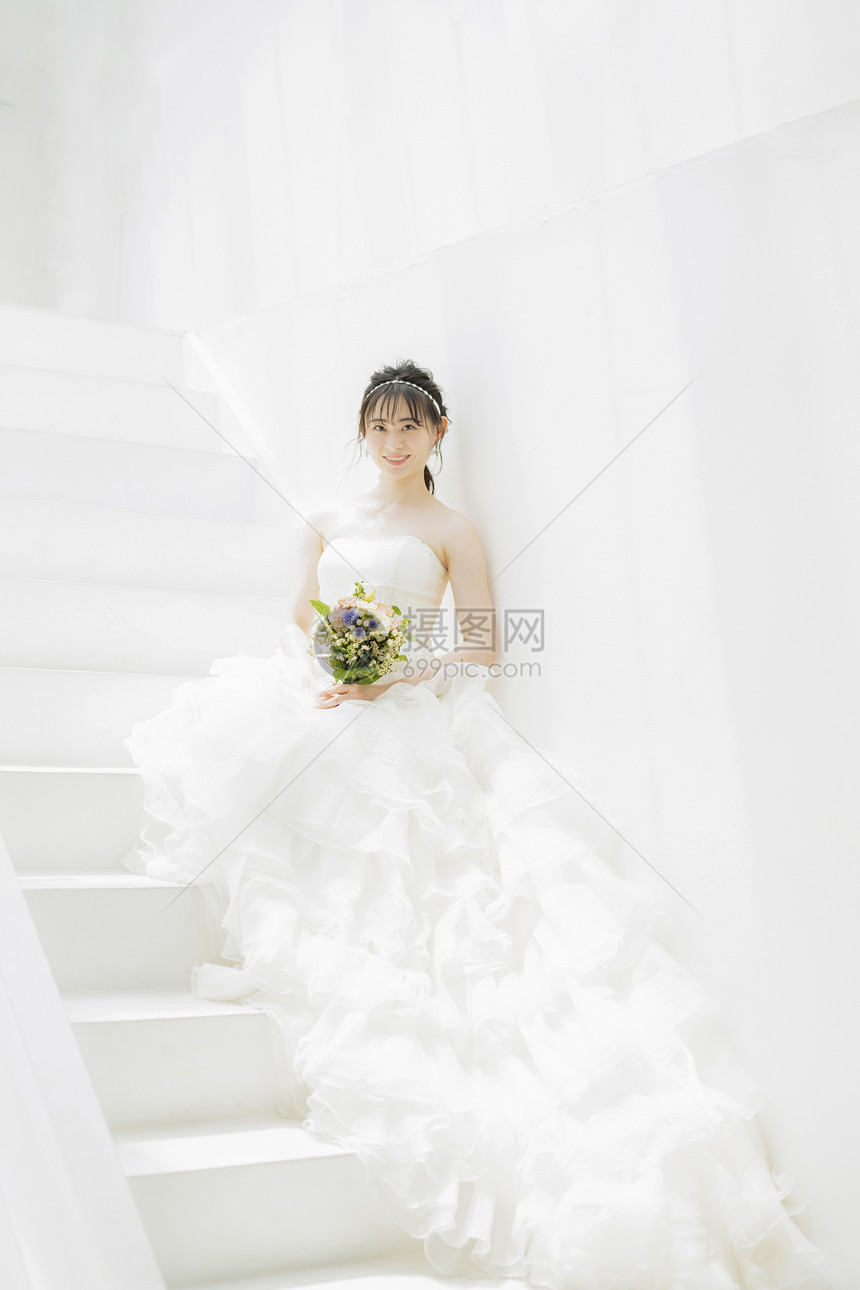 坐在台阶上拿着手捧花的婚纱美女图片
