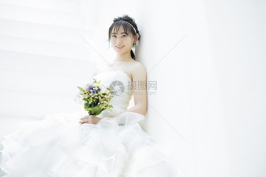 靠在墙上手拿捧花的婚纱美女图片