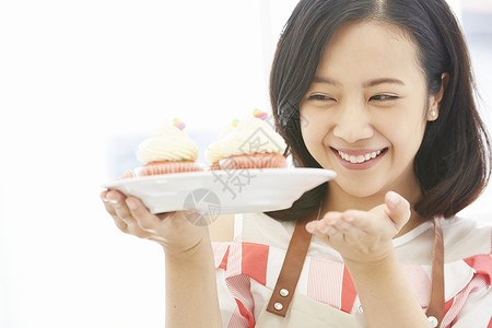 年轻女子端着杯子蛋糕开心的微笑图片