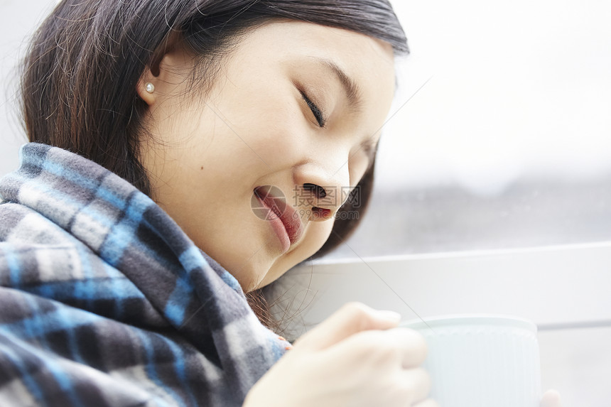 裹着围巾拿着咖啡放松的年轻女子图片