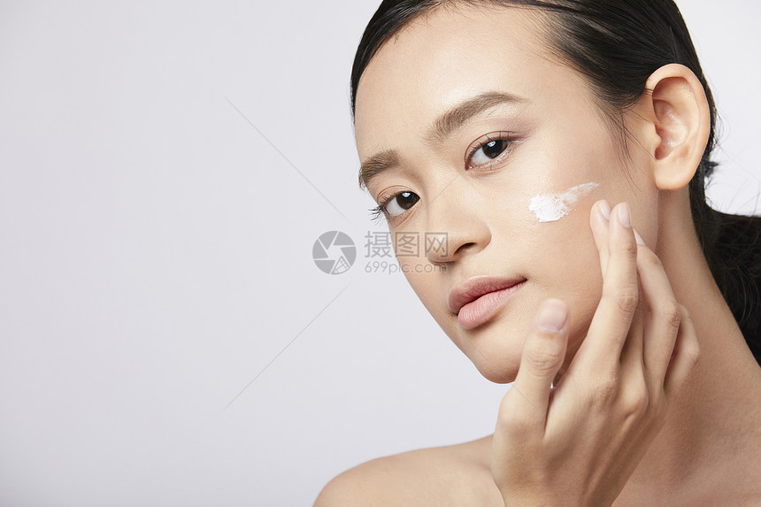 脸部护肤涂抹乳液的年轻女子图片
