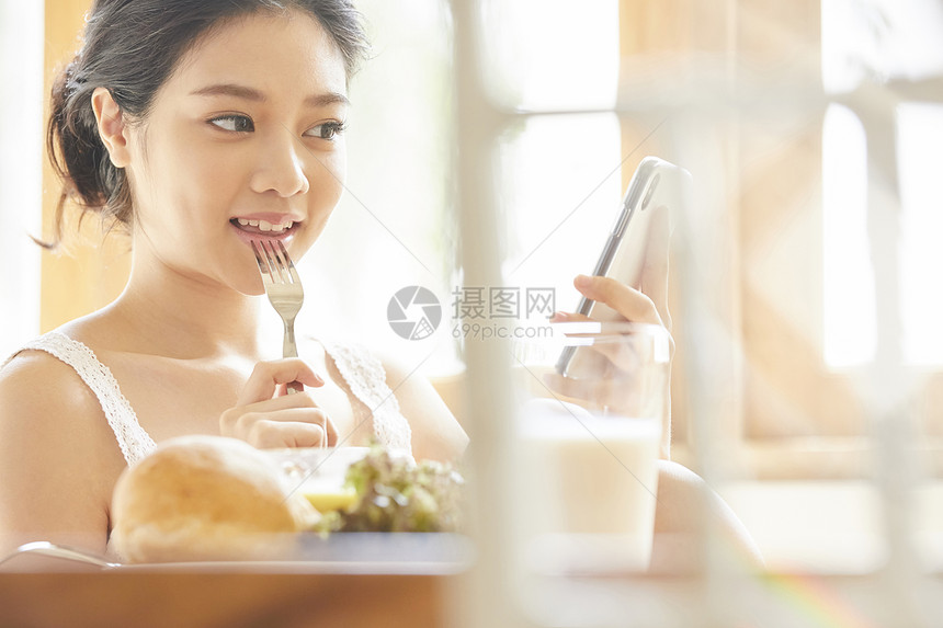 吃早餐看着手机的年轻女子图片