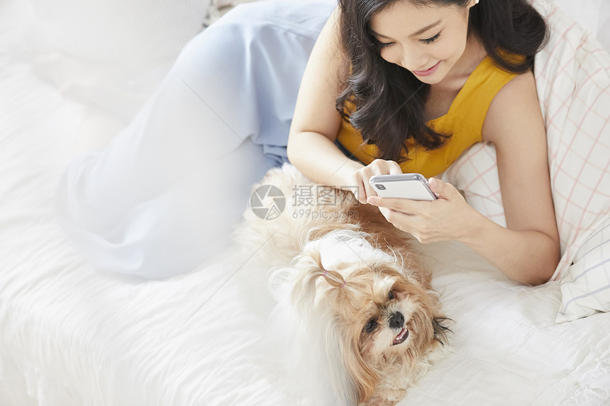 床上抱着宠物狗看手机的年轻女子图片