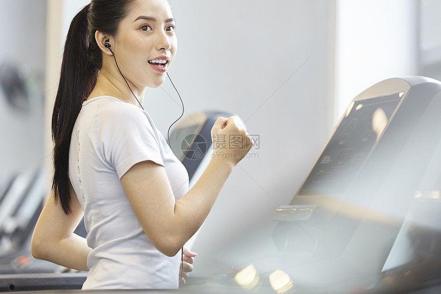 戴着耳机跑步机上运动的女青年图片