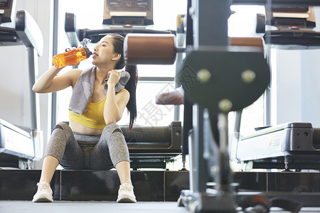 健身房坐着喝水休息的年轻女子图片