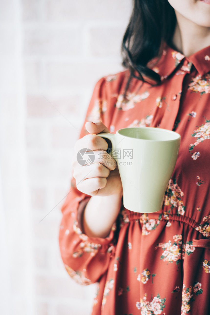 站立在与杯子的窗口的一个红色一件妇女的手图片