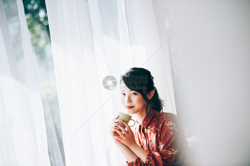 假日坐在靠窗的沙发上喝茶的女人图片