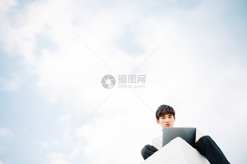 一个男人坐在屋顶上打开笔记本电脑图片