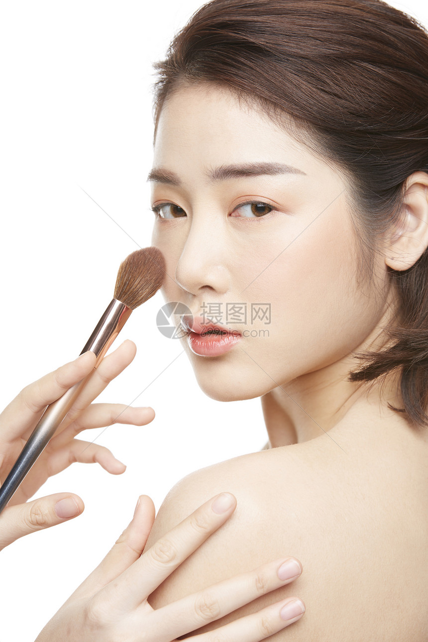 化妆刷轻扫面颊的美妆女性图片