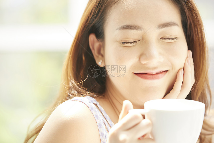拿着咖啡捧脸微笑的年轻女子图片