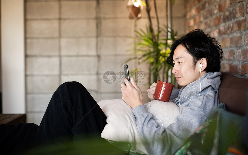 居家看着手机喝咖啡的男青年图片