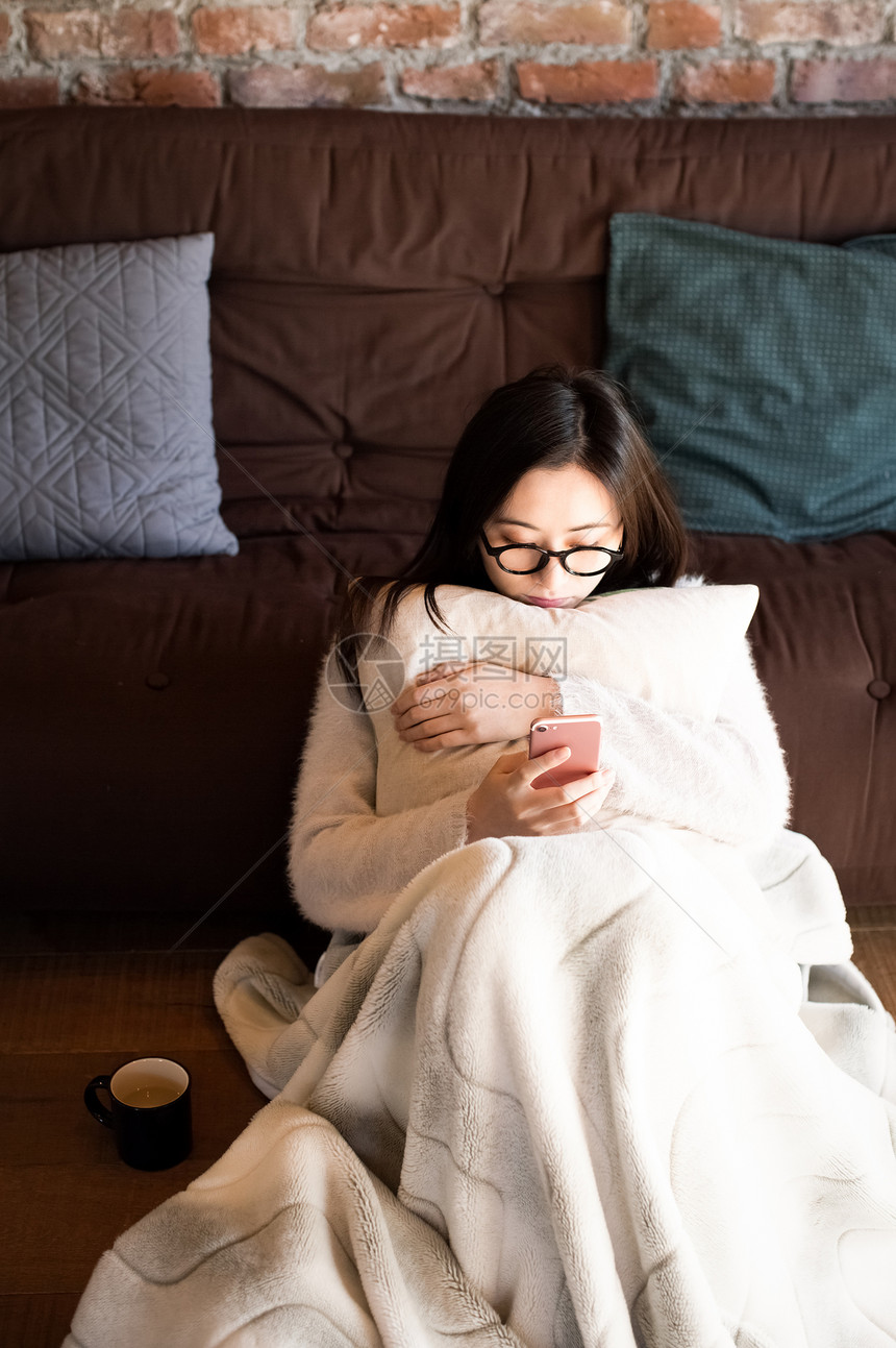 居家抱着抱枕看手机的女青年图片