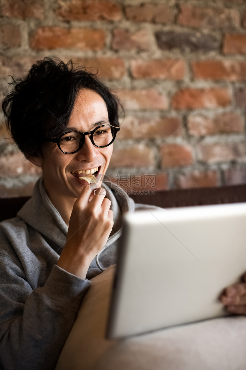 看着平板电脑吃零食的成年男子图片