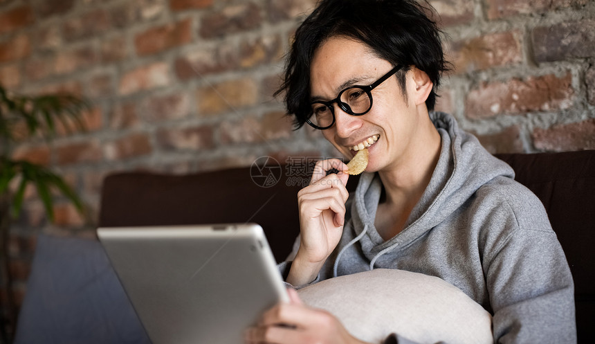 看着平板电脑吃零食的男性图片