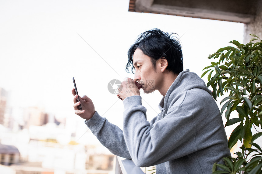 户外阳台喝咖啡看手机的男青年图片
