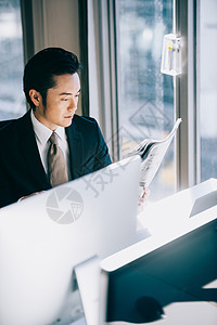 年轻经理资料读一张报纸的上司人在个人计算机在窗口的一个位子图片