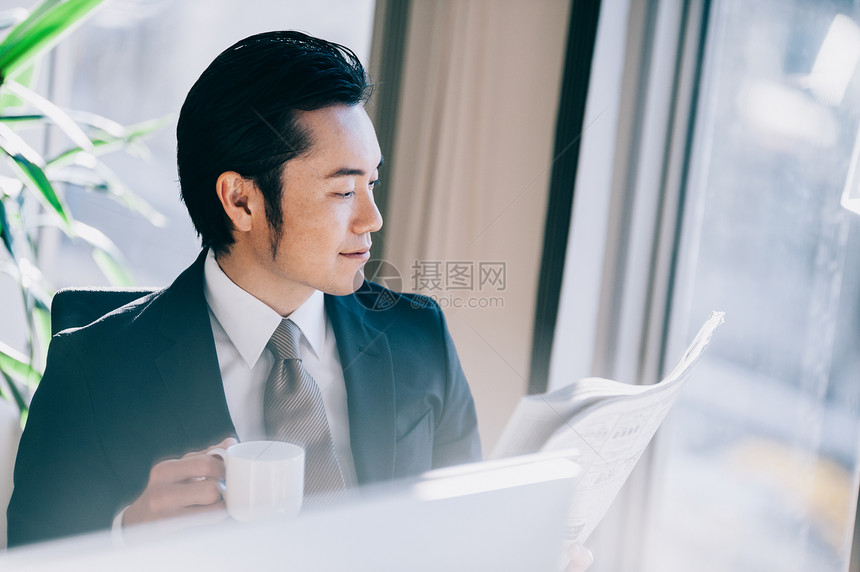 市场营销壮年笑脸读一张报纸的上司人在个人计算机在窗口的一个位子图片