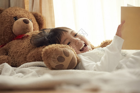 室内抱玩具熊的女孩在床上图片