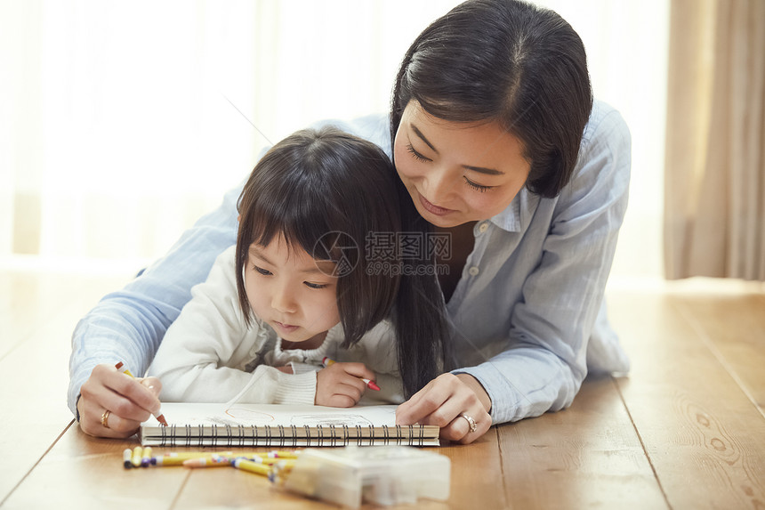 少女较年轻微笑帮助女儿的母亲在客厅的地板上画图片