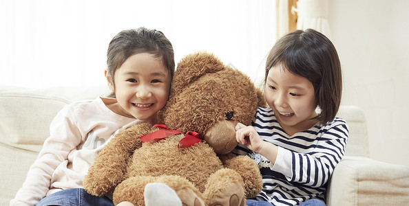 四岁年轻的女孩两个人姐妹们在沙发上玩大熊图片