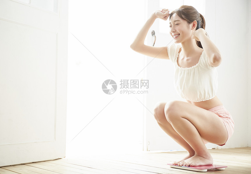 蹲在体重秤上开心的年轻女子图片
