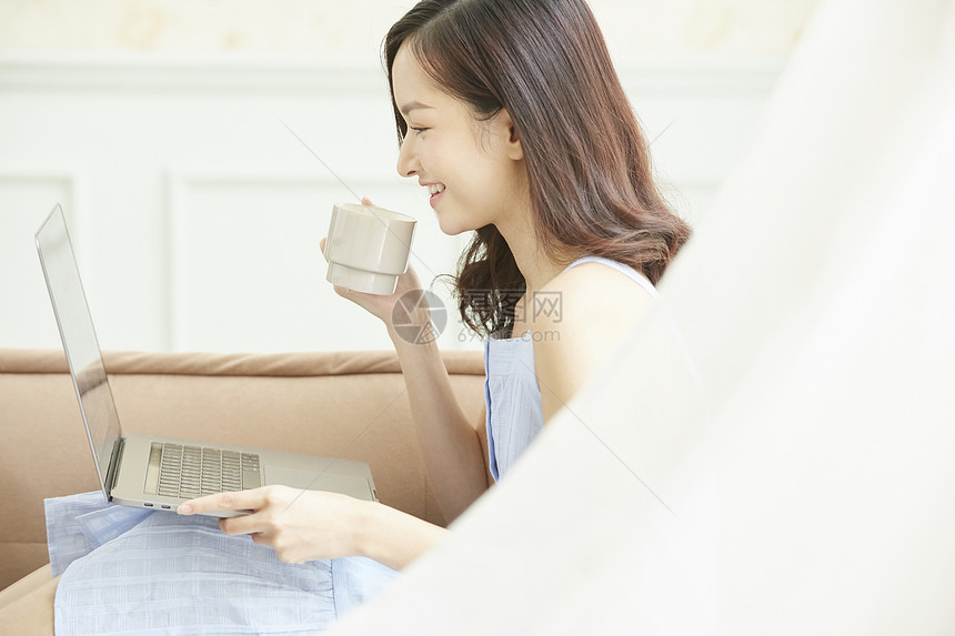 拿着咖啡使用电脑的女青年图片