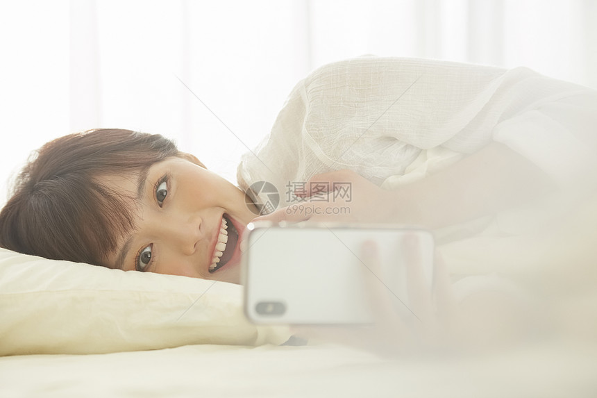可爱女生开心的在床上看手机图片