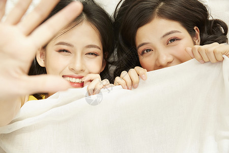 两个年轻女人开心躺在被子里双胞胎中的高清图片素材
