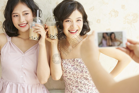 年轻姐妹淘端着奶茶拍照合影笑容高清图片素材