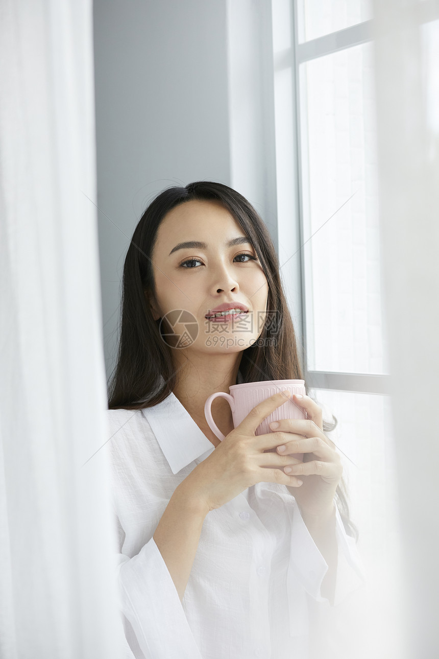 窗边捧着水杯的年轻女子图片