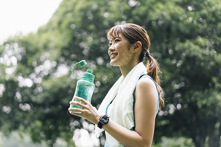 靠着水瓶的女孩拿着水瓶喝水休息的运动女青年背景
