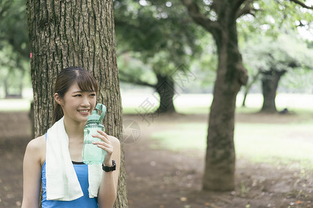 户外靠在树上喝水休息的青年女子图片