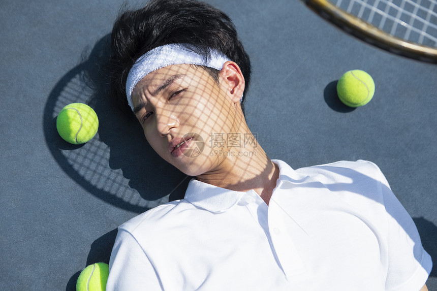 青年男子躺在网球场上休息图片