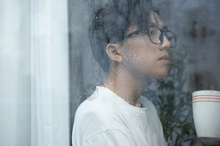 下雨天站在窗边喝咖啡的青年男子图片
