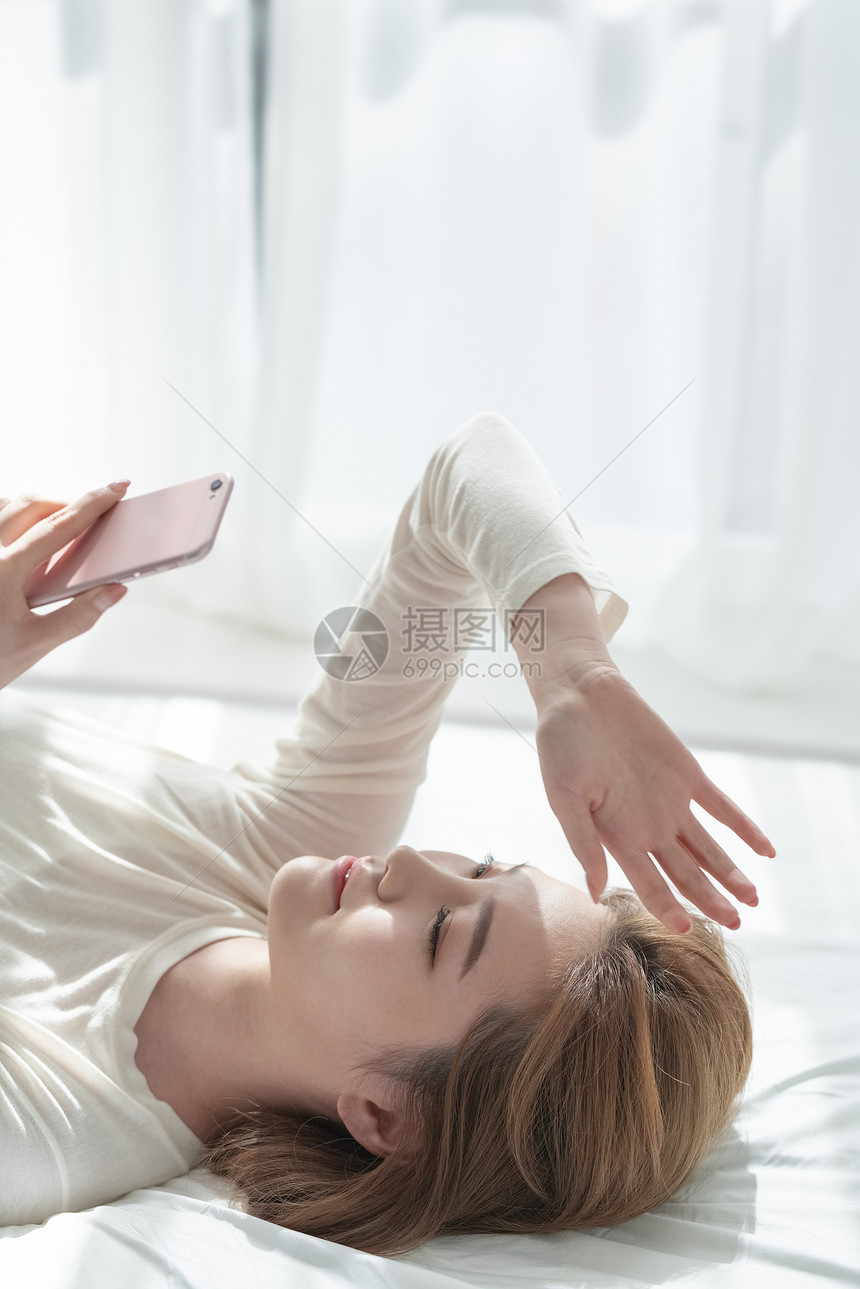 躺在床上玩手机的青年女子图片