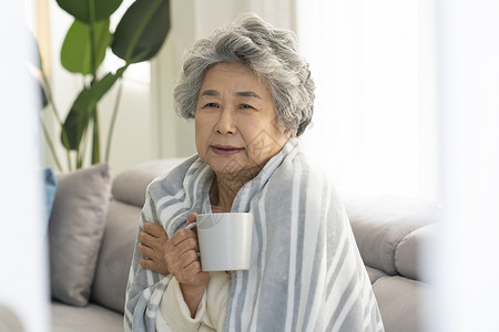 裹着毛毯生病喝水的老年女性图片