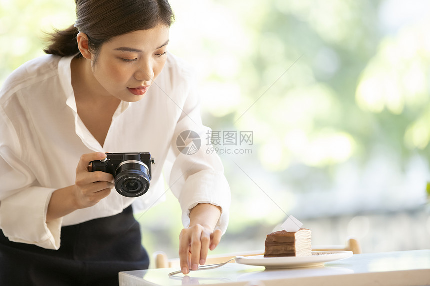 拿着相机拍甜品照片的年轻女子图片