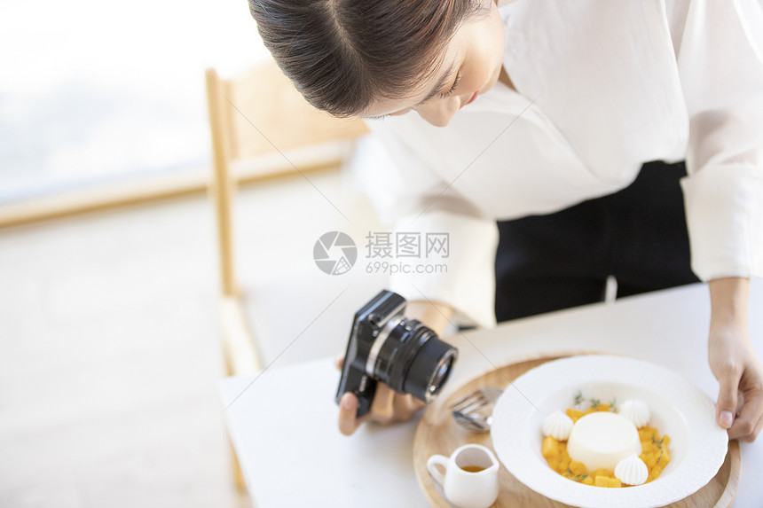 年轻女子拿着相机拍摄食物照片图片