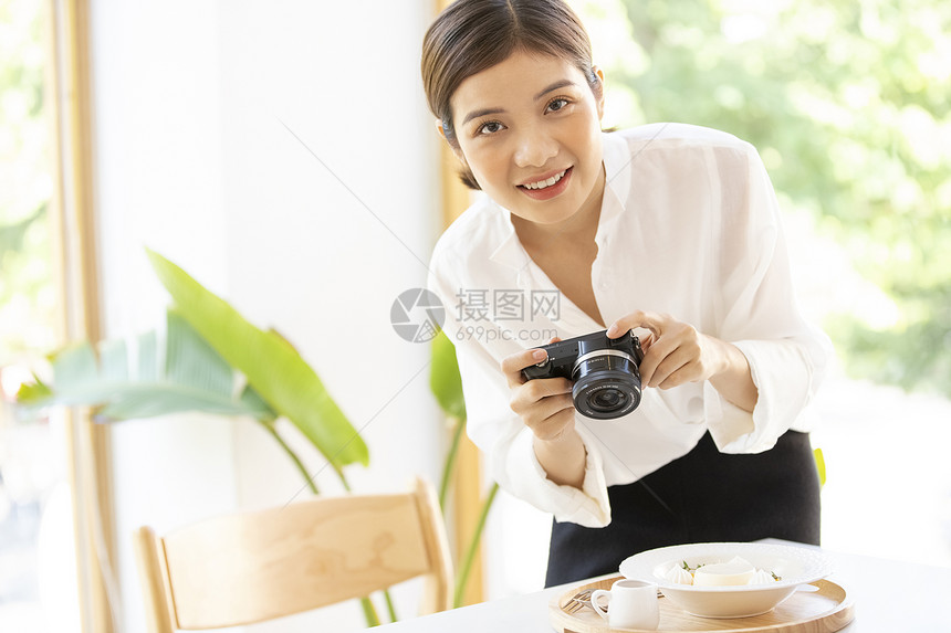 年轻女子拿着相机拍食物照片图片