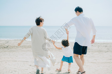 海滩上手牵手散步的一家三口背影图片