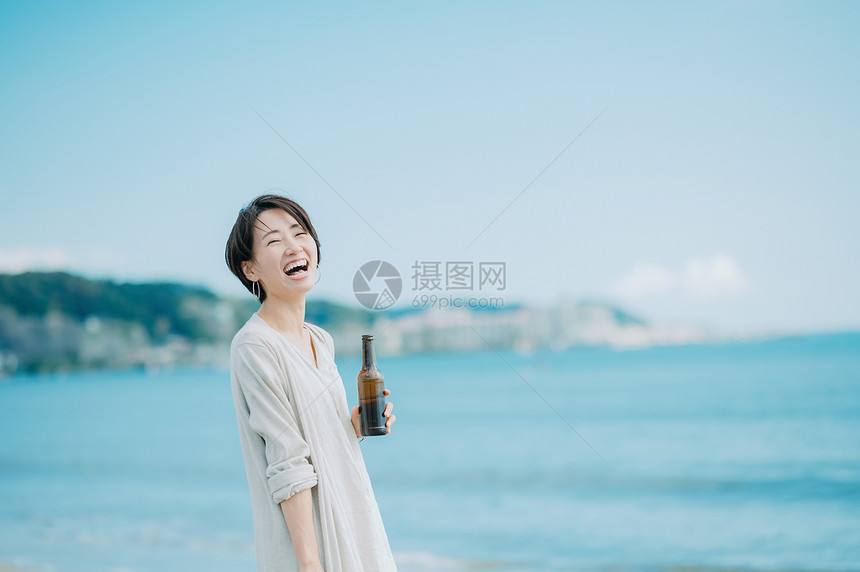 海边拿着啤酒开心的青年女性图片