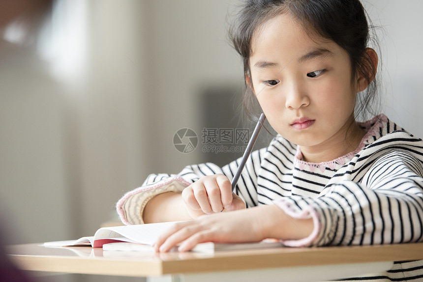 小女孩坐在课桌上认真写作业图片