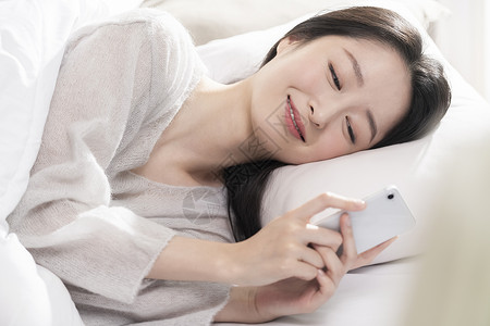 青年女子床上玩手机微笑背景图片