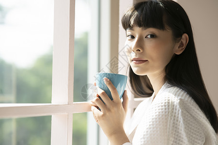 窗边捧着咖啡的年轻女子图片