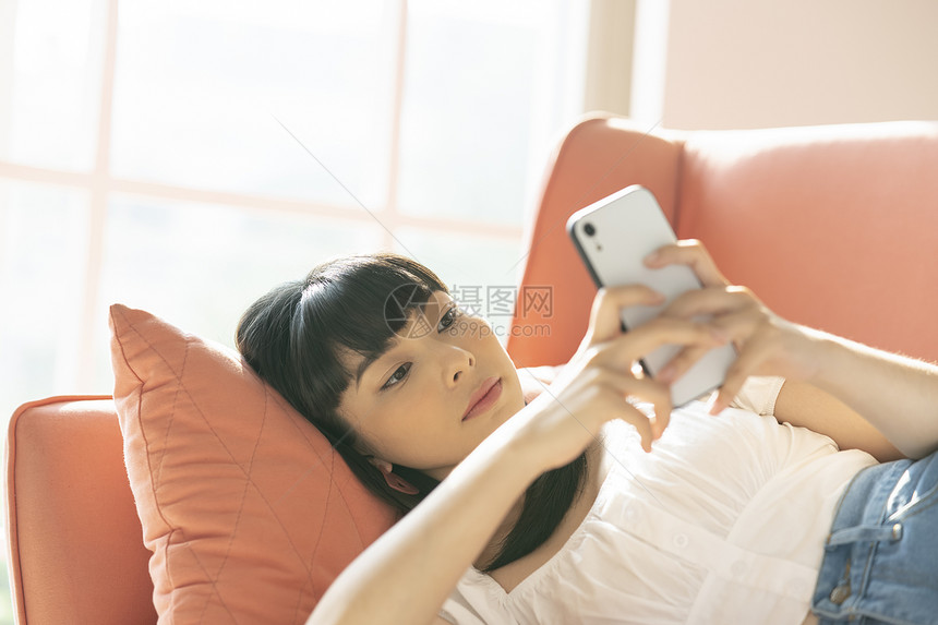 青年女子躺在沙发上玩手机图片
