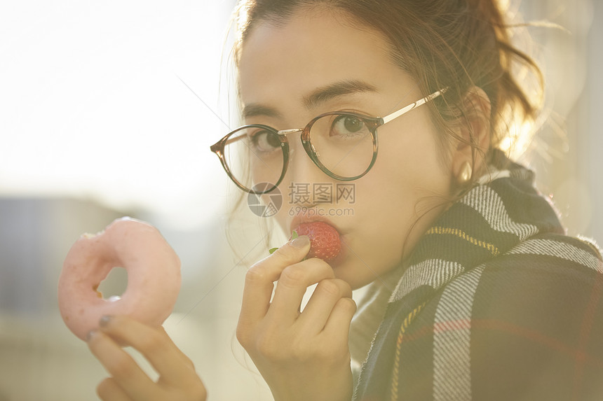 拿着甜甜圈吃草莓的年轻女子图片