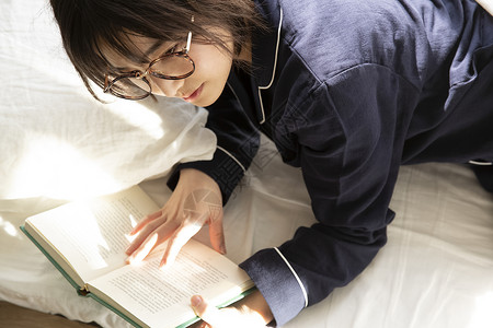 床上翻开书阅读的年轻女子图片