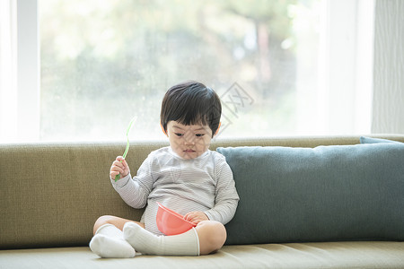 沙发上拿着勺子和碗的小男孩图片