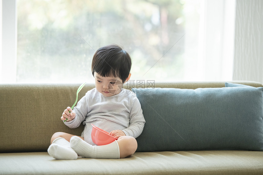 沙发上拿着勺子和碗的小男孩图片