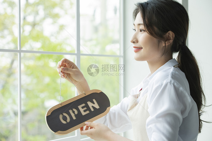 挂上开门标牌的年轻女店员图片